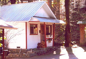 A two-bedroom cabin with a blue metal roof and firewood stacked by the door